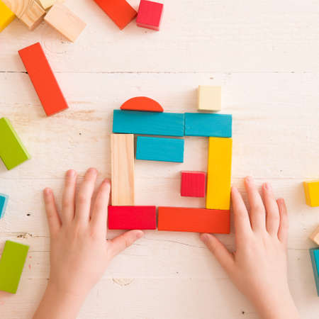 Top view on child's hands playing with colorful wooden bricks on the white table background.Kid...
