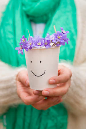 Woman holding beautiful snowdrops in a paper cup. first spring flowers in a forest. Wild flowers. spring concept.の写真素材