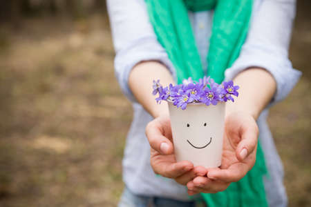 Woman holding beautiful snowdrops in a paper cup. first spring flowers in a forest. Wild flowers. spring concept.の写真素材