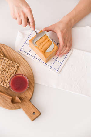 Top view on woman's hands cutting traditional scandinavian organic brown cheese with cheese knife on kitchen table. Healthy Breakfast or snack. Healthy food and eating.の写真素材