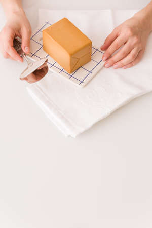 Top view on woman's hands cutting traditional scandinavian organic brown cheese with cheese knife on kitchen table. Healthy Breakfast or snack. Healthy food and eating.の写真素材