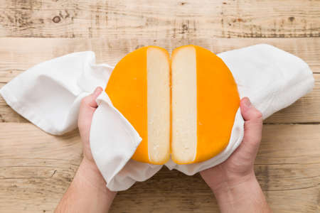 Top view on cut cheese head in yellow vacuum pakage in man's hands on wooden board. Serving French...