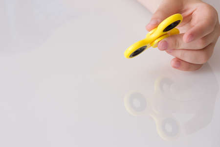 Child's hand spinning a fidget spinner device. Top view. Playing with a yellow hand spinner fidget toyの写真素材