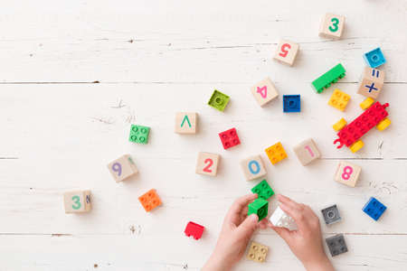 Top view on child's hands playing with wooden cubes with numbers and colorful toy bricks on white wooden background. Baby with toysの写真素材