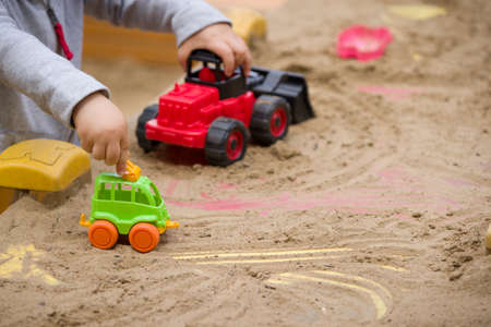 Portrait of cute toddler boy sitting on the ground and playing with toy tractor and sand in the park. Child walking outdoors. Lifestyle.の写真素材