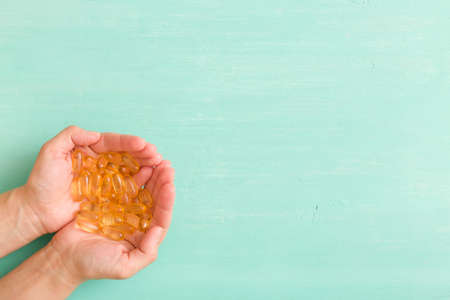 Top view on woman's hands holding pile of capsules Omega 3 on turquoise background.の写真素材