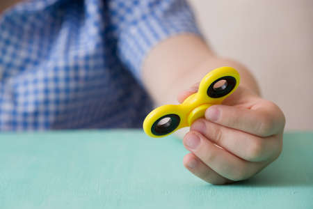 Child's hand spinning a fidget spinner device. Playing with a yellow hand spinner fidget toyの写真素材