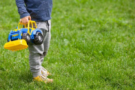 Closeup of toddlers hands holding colorful toy tractor while standing on green grass in the park.の写真素材