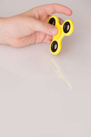 Child's hand spinning a fidget spinner device. Top view. Playing with a yellow hand spinner fidget toyの写真素材