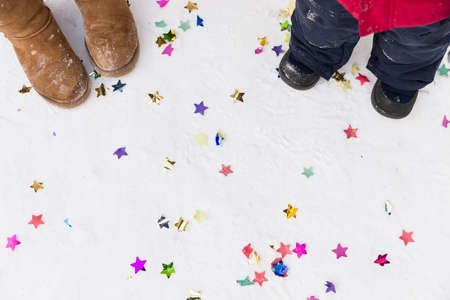 Top view on woman's and child's feet on the snow ground with confetti. Holidays, winter and Christmas. Outdoor. Family celebrating.の写真素材