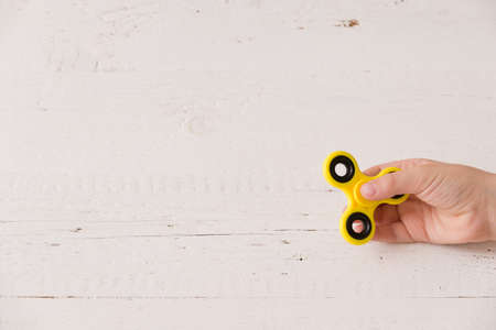 Child's hand spinning a fidget spinner device. Top view. Playing with a yellow hand spinner fidget toyの写真素材