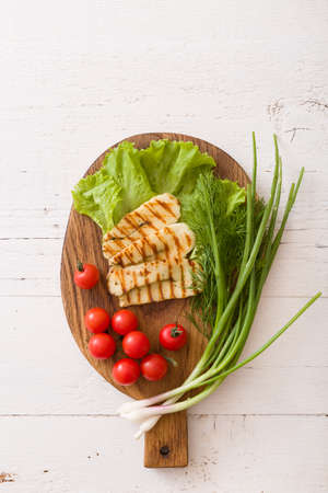 Grilled slices of homemade halloumi cheese with green salad, fresh herbs and organic tomatoes. Fried halloumi cheese with grill marks on wooden background, top view, close-upの写真素材