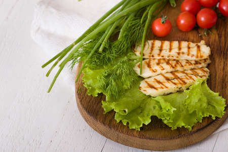 Grilled slices of homemade halloumi cheese with green salad, fresh herbs and organic tomatoes.Fried halloumi cheese with grill marks on white wooden background, top viewの写真素材