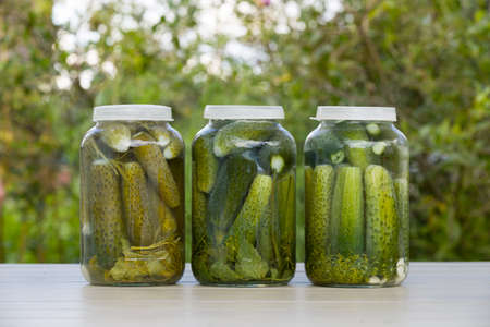 Closeup of canned cucumbers in three glass jars on the table in the garden.Outdoors. Pickled...