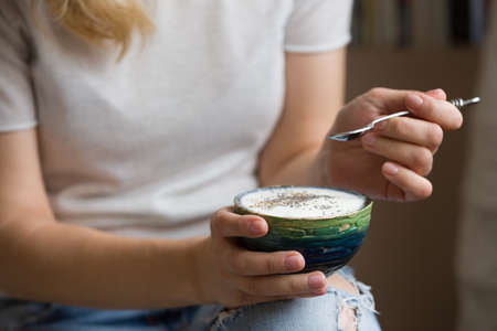Closeup of woman's hands holding cup with organic yogurt with blueberries, coconut and fresh mint. Homemade vanilla yogurt in girl's hands. Breakfast, snack. Healthy eating and lifestyle conceptの写真素材