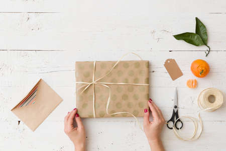 Top view on girl's hands wrapping Christmas or birthday gift in craft paper and decorating with ribbon and tag. Preparing present and card for celebration. Holidays seasonの写真素材