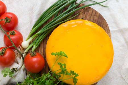 Homemade organic cheese head in yellow vacuum package with Tomatoes, Basil, onions herbs on wooden board on the table. Healthy food, snack and eating.の写真素材