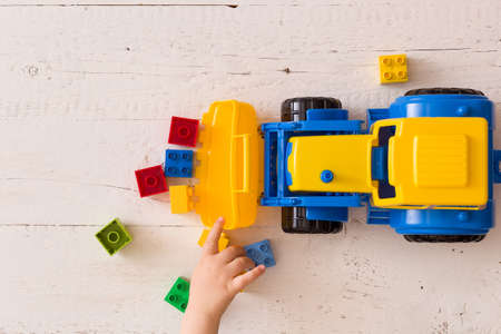 Closeup of toddler boy's hands playing with colorful toy tractor. Child playing with a car at a nursery or preschool.の写真素材
