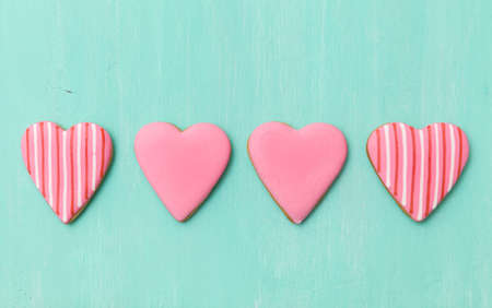 Top view on four pink sugar cookies in heart shape on turquoise wooden background. Valentine's day card.の写真素材