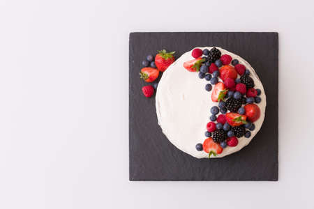 Top view on homemade vanilla birthday cake decorated with berries: strawberries, blueberries, raspberries on black board. Celebration, party cake.の写真素材