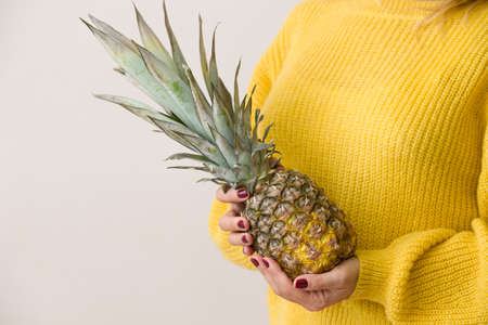 Closeup of a juicy pineapple in hands of woman on yellow sweater background. Healthy food.の写真素材