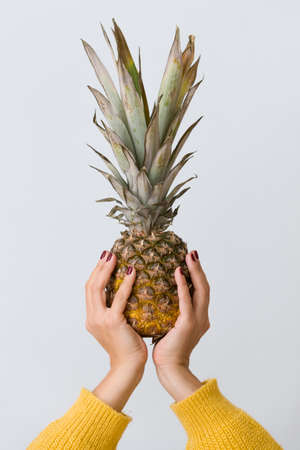Closeup of fresh pineapple in woman's hands on light blue background.の写真素材