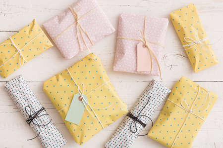 Top view on small gifts wrapped in colorful paper with ribbons and tags on white wooden background....