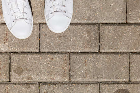 top view on white sneakers on pavement tiles. Woman's shoes on asphalt on sunny summer day.の写真素材