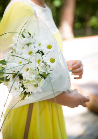Closeup of beautiful bunch of garden chamomiles in woman's hands. Girl in yellow dress with summer flowers on sunny summer day.の写真素材
