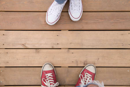 Top view on two people's feet in white and red sneakers standing on wooden floor or bridge.の写真素材