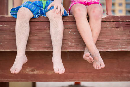 Small children sitting on the wooden pier in the water and enjoying summer day. Bare feet of boy and girl. Vacation by the sea. Outdoors. Siblings. Sister and brother by the ocean.の写真素材