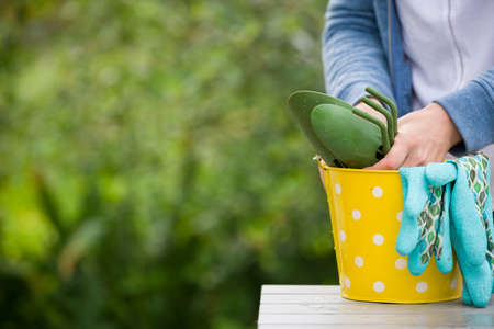 closeup of woman's hands holding yellow metal bucket with rubber gloves and garden tools on nature background. Girl in the garden.の写真素材