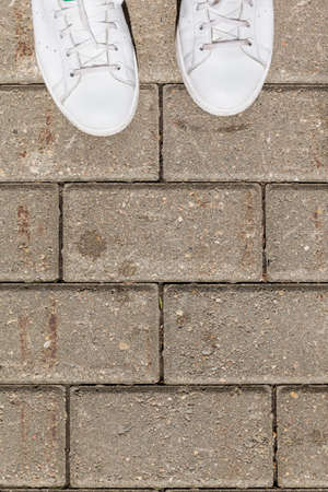 top view on white sneakers on pavement tiles. Woman's shoes on asphalt on sunny summer day.