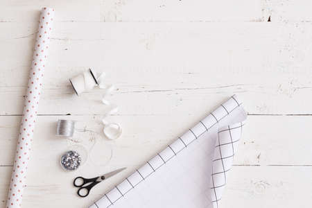 Top view on rolls of black and white paper  with ribbons, decorations and scissors on white wooden...