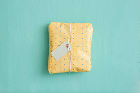 Top view on gift wrapped in yellow paper with dots on turquoise wooden background.の写真素材