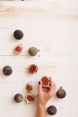 Top view on girl's hand taking sliced figs from white wooden table or background. Healthy snack and food.の写真素材