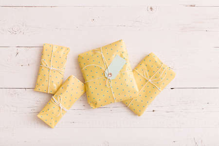 Top view on small gifts wrapped in yellow paper with ribbons and tag on white wooden background....