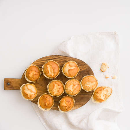Top view on wooden board with freshly baked home muffins on white table background.