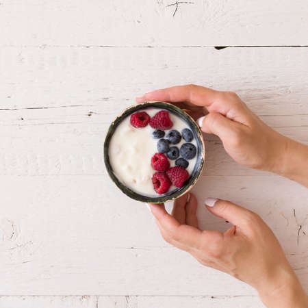Top view on bowl with yogurt and berries on girl's hands. Healthy eating concept