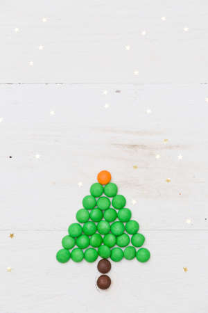 Top view on a small funny Christmas tree made of candies with golden stars confetti on white wooden background. Christmas and Happy New Year conceptの写真素材