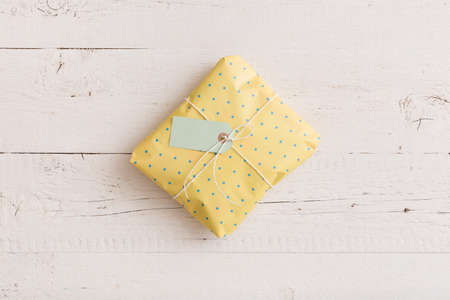 Top view on small wrapped gift with ribbons and tag on white wooden background. Present for...