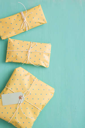 Top view on small gifts wrapped in yellow paper with ribbons and tags on turquoise wooden...