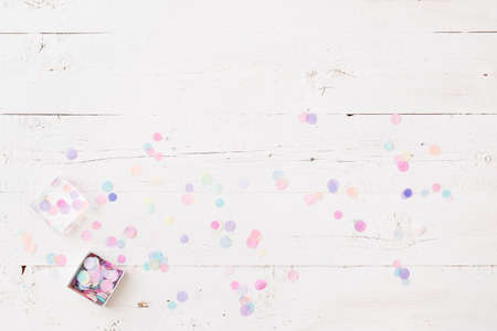 Top view on box full of colorful confetti on white wooden table or background.