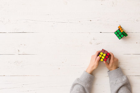Moscow, Russia, February 16 2018: Rubik's cube in girl's hands on white wooden background. Girl holding Rubik's puzzle toy and playing with it.のeditorial素材