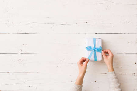 Girl's hands holding beautiful Christmas or birthday gift wrapped in white paper on white wooden background. Top viewの写真素材
