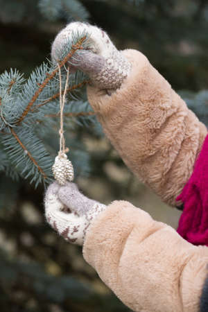 Closeup of young woman's hands near a Christmas tree with decorations on a cold winter day.の写真素材