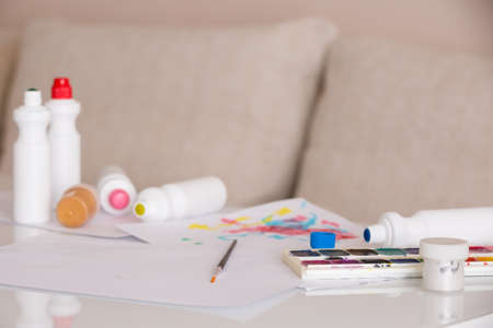 Paints, brushes, paper and other stationary supplies on the white table. Hobby.