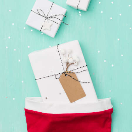 Closeup of nice Christmas gifts wrapped in white paper, Christmas tree decorations,  Santa's hat on...