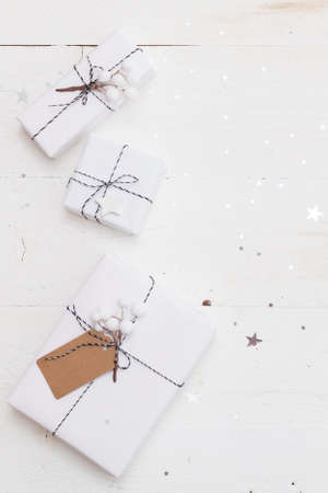 Closeup of nice Christmas gifts wrapped in white paper and decorated with twine on old white wooden background with shiny silver stars and decorations. Holidays concept.の写真素材