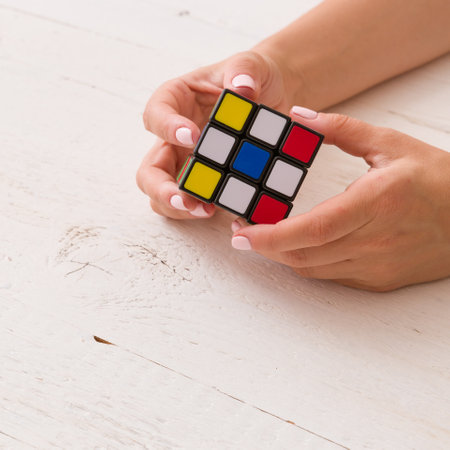 Moscow, Russia, August 16 2017: Closeup of colorful cube in woman's hands. Girl holding colored Rubick's cube and playing with it on old wooden background.のeditorial素材